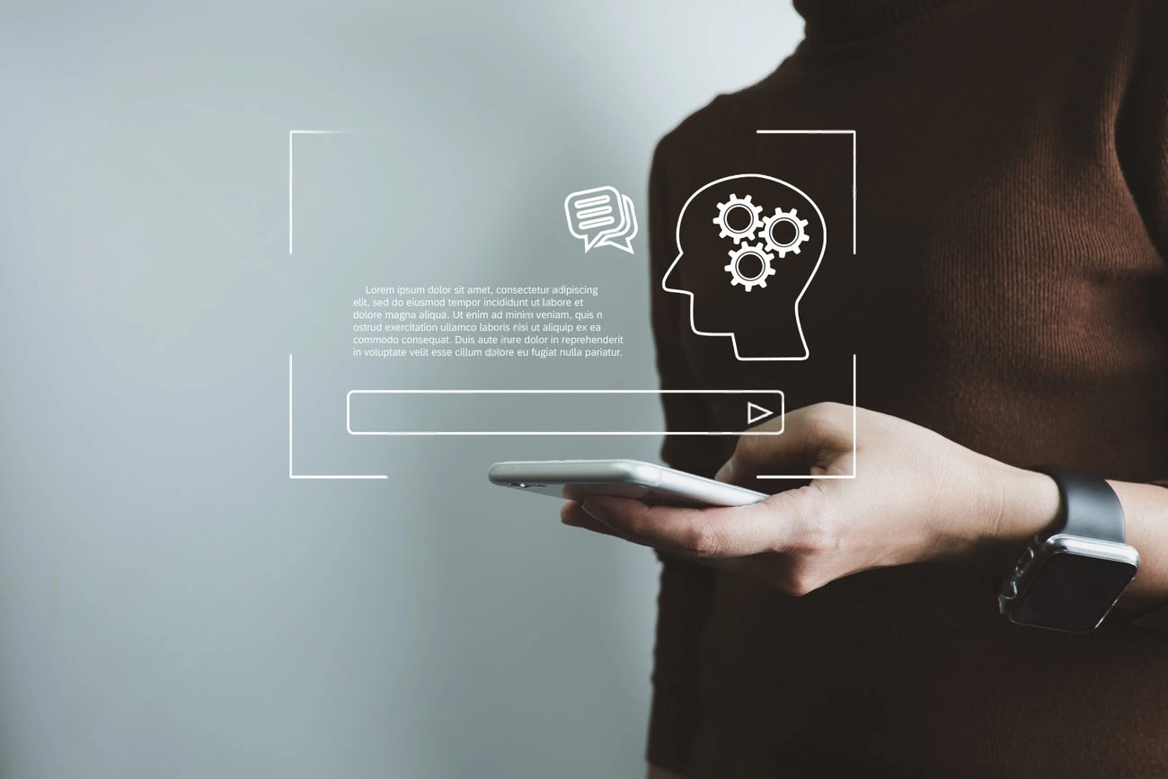 Person holding a smartphone with digital icons of a head, gears, and a chat bubble overlayed, suggesting technology, communication, artificial intelligence, and the convenience of using tools like a caption generator.