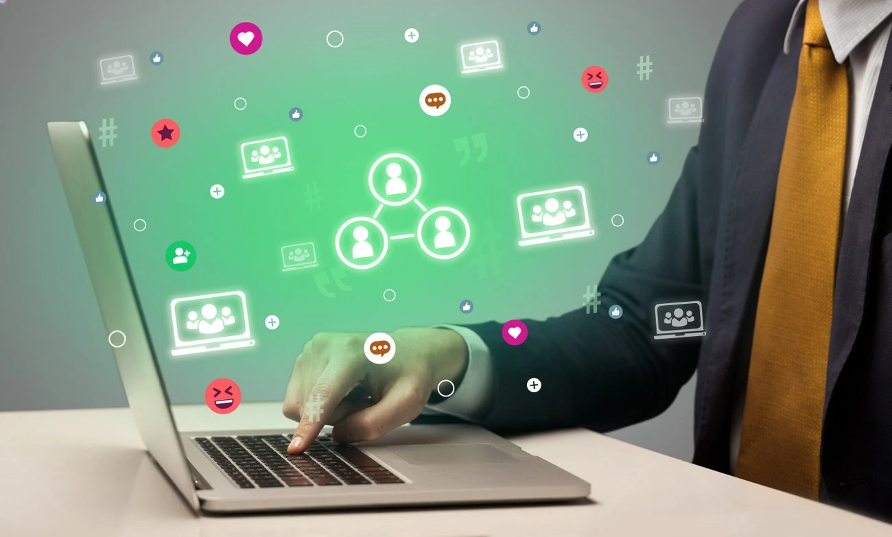 A person in business attire uses a laptop, with digital social network and communication icons floating above the screen, showcasing the power of a caption generator in professional networking.
