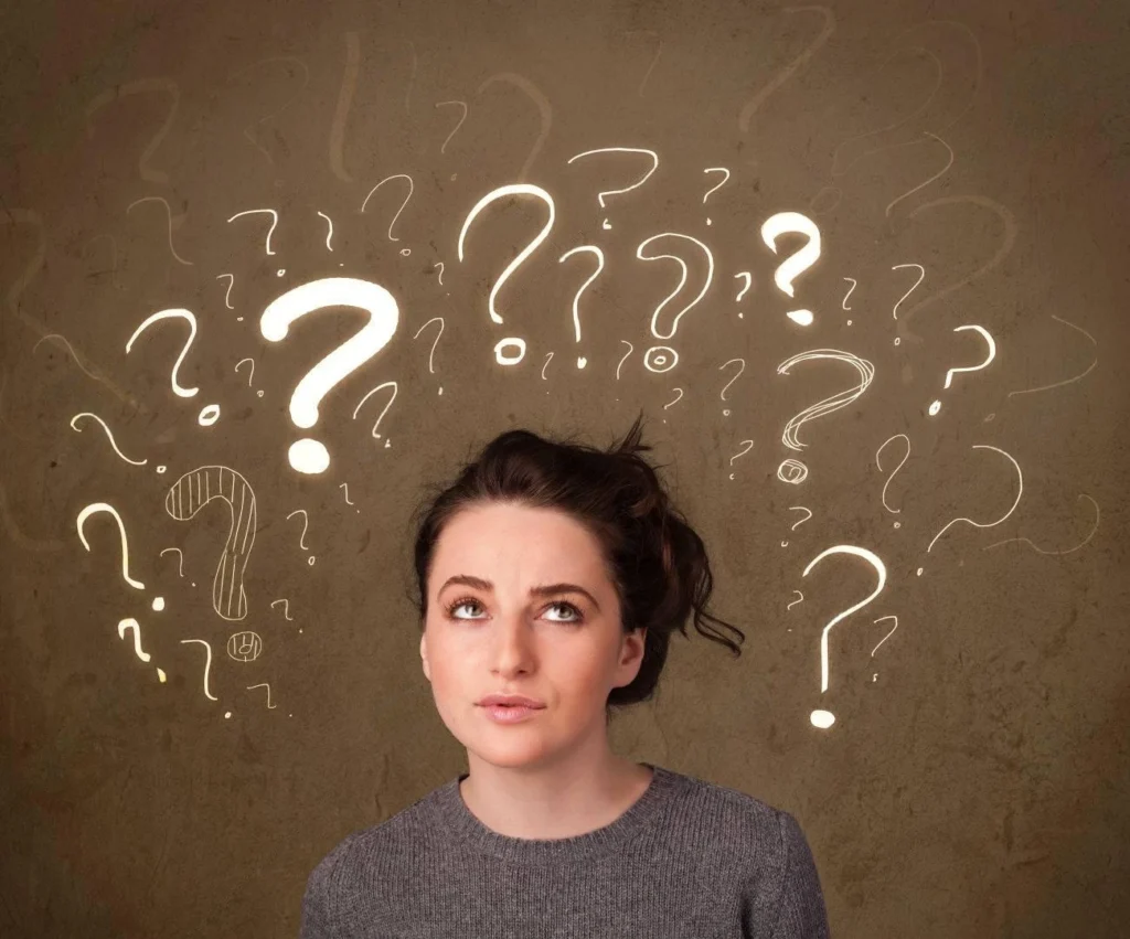 A woman looks upward with a thoughtful expression as multiple illuminated question marks appear around her on a brown background&mdash;perfect inspiration for clever IG captions.