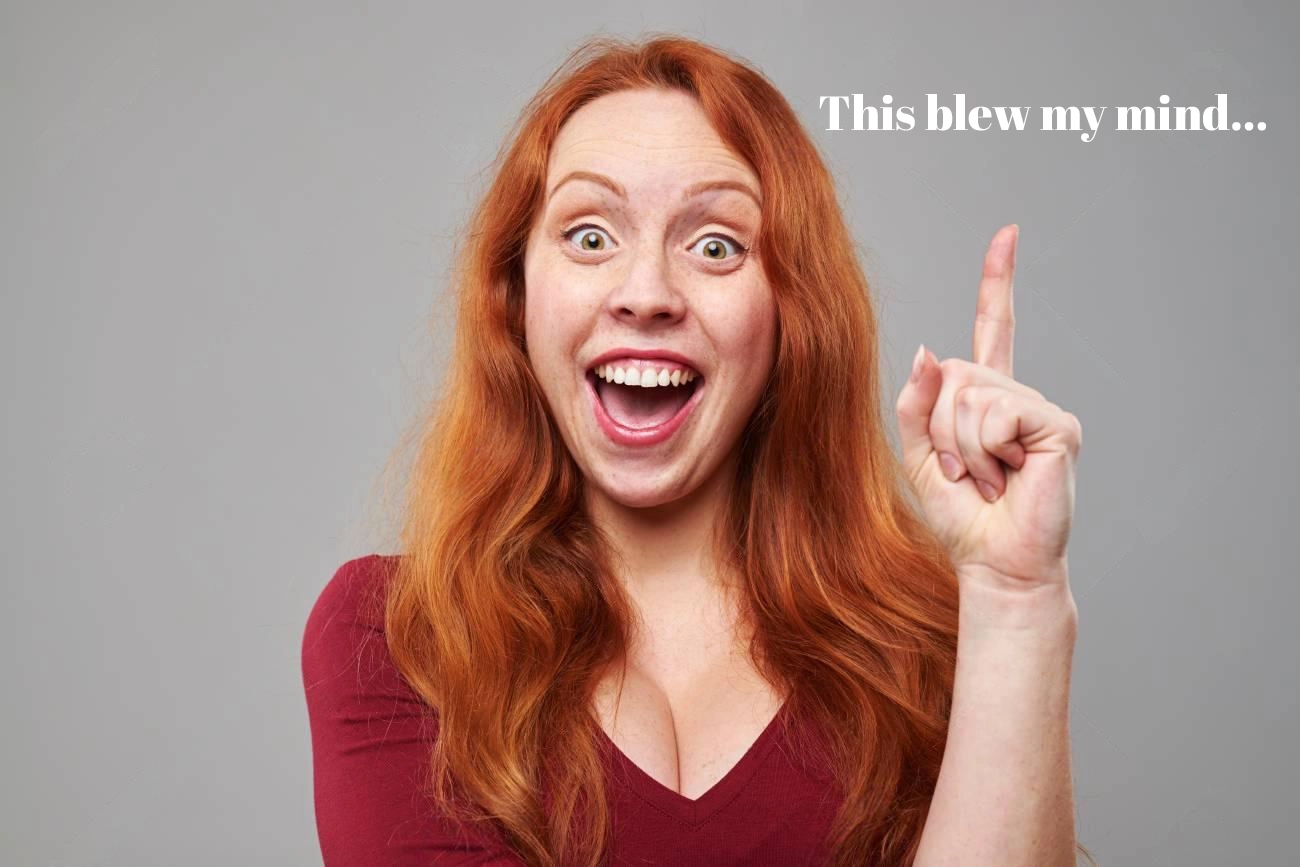 A woman with long red hair and a maroon shirt smiles widely and points upward; white text reads, "This blew my mind... IG Captions" on a plain gray background.