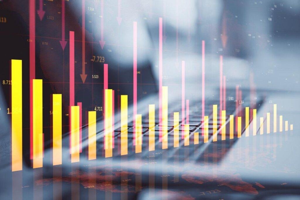 Describe a Picture: Bar and line charts with downward red arrows are superimposed on a blurred image of hands typing on a keyboard, illustrating a decline in financial or market data.