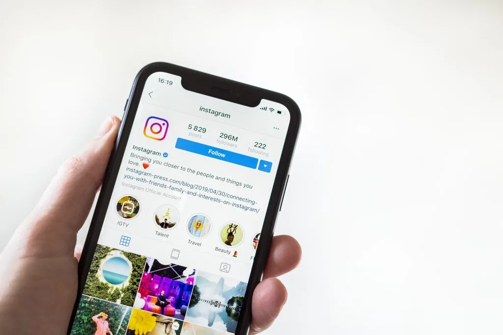 A hand holding a smartphone displays the official Instagram profile page, featuring follower count, profile details, and story highlights on the Instagram app.