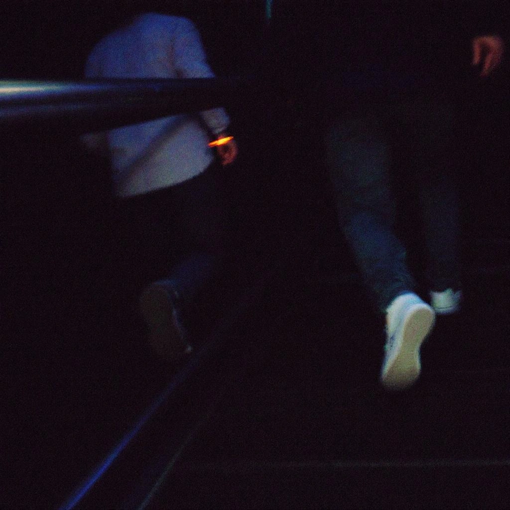 Two people are walking up a dark staircase; one in a light shirt, the other in a dark outfit, both partially out of frame&mdash;an intriguing scene that exemplifies detailed image descriptions.
